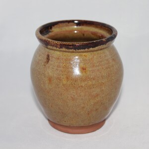 May include: A small, round, ceramic vase with a brown rim and a speckled, light brown glaze.