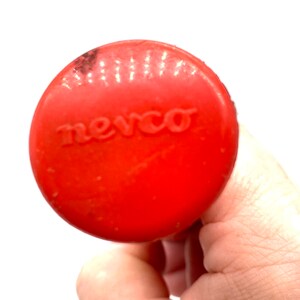 Op de afbeelding: Close-up van een rode plastic flesdop met het woord "newco" erop gegraveerd.
