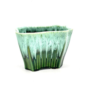 May include: A green and white glazed ceramic planter with an irregular, wavy rim. The planter has a textured, drip-like glaze pattern.