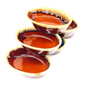 May include: Set of four brown and cream glazed oval ceramic baking dishes. The dishes are stacked on top of each other.