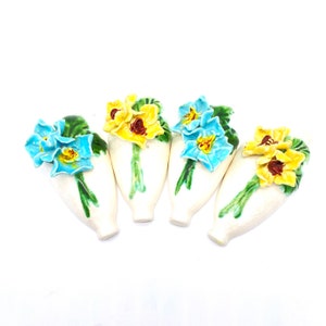 May include: Set of four ceramic wall vases with floral designs. Each vase features a bouquet of blue and yellow flowers with green leaves.