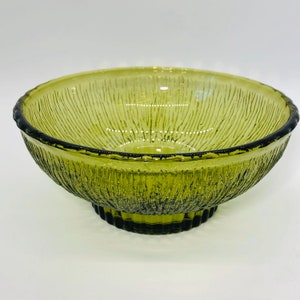 May include: A green glass bowl with a textured, ribbed design. The bowl has a wide, shallow base and a flared rim.