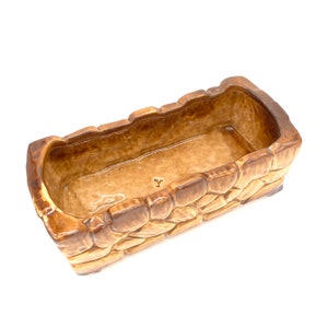 May include: A brown ceramic planter shaped like a stone wall. The planter has a rectangular shape and is approximately 10 inches long. The planter has a smooth, glazed finish.