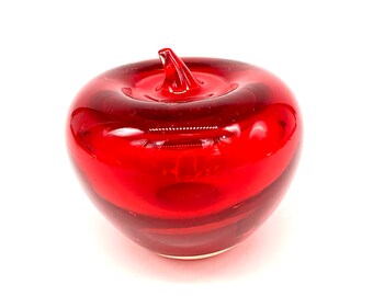 May include: A red glass apple paperweight. The apple is made of clear glass with a red tint. The apple has a stem and a leaf.