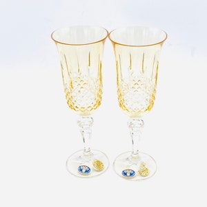 Puede incluir: Dos copas de champán transparentes de color ámbar con un patrón de diamante. Las copas están sobre una superficie blanca y tienen una pegatina dorada en la parte inferior que dice "BOHEMIA CRYSTAL".