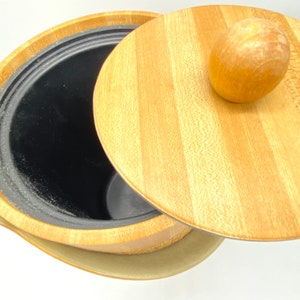 May include: A wooden ice bucket with a lid and a knob on top. The bucket is made of light brown wood with a dark brown interior. The lid is also made of wood and has a striped pattern.