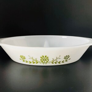 May include: White oval serving dish with a green floral pattern. The dish has two handles and a divider in the center. The floral design features stylized green flowers and leaves. The dish is likely made of ceramic or glass.