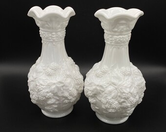 Puede incluir: Dos jarrones de vidrio de leche blanco con un diseño en relieve de uvas y hojas. Los jarrones miden aproximadamente 20 cm de alto.