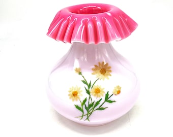 May include: A small, white glass vase with a pink ruffled top and a floral design of yellow daisies.