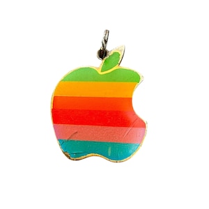 May include: A vintage Apple logo pendant in the shape of an apple, featuring a rainbow stripe design. The pendant has a silver-colored bail for attaching to a chain. The apple design is a classic retro style.