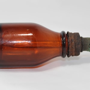 May include: A small, amber glass bottle with a dropper. The bottle has a black rim and a rusty metal cap with a green rubber tip.