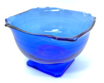 Peut inclure: Un bol en verre bleu cobalt avec une base carrée et un bord ondulé. Le bol est en verre transparent avec une teinte bleue.