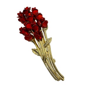 Può includere: Spilla dorata a forma di bouquet di rose rosse. Le rose hanno una finitura lucida, e gli steli e le foglie presentano un design strutturato. Un accessorio classico.