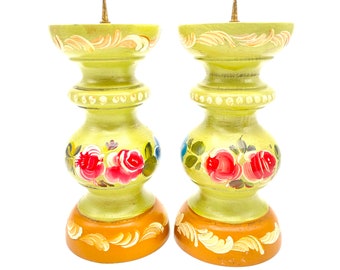 May include: A pair of hand-painted wooden candle holders with floral designs. The candle holders are green with gold accents and feature red, pink, and blue flowers.