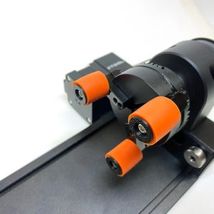 May include: A black and orange 3D printer with three orange wheels. The printer is on a black platform.