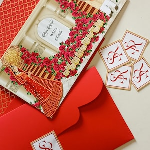 Peut inclure: Un ensemble de faire-part de mariage avec une carte décorative représentant un couple, des roses rouges et le texte "Raja Afzal Weds Sahdia". L'ensemble comprend des enveloppes rouges, une carte à motifs et de petites cartes carrées avec des initiales.