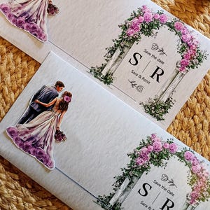 Peut inclure: Deux cartons d'invitation de mariage avec un motif d'arche florale et le texte "Save the date". Les cartes présentent une illustration de couple et les initiales "S R". L'arche est ornée de roses roses et de verdure.