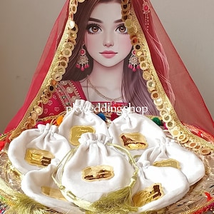 May include: A wedding gift set with white drawstring pouches, each with a gold label, presented on a decorated tray. The tray has colourful trim and tassels. A red veil with gold detailing and a woman's portrait are in the background.