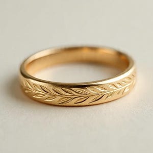 Può includere: Un anello color oro con un motivo a foglie dettagliato che circonda la fascia. L'anello ha una finitura lucida e un design classico. L'anello è probabilmente in oro ed è adatto all'uso quotidiano.