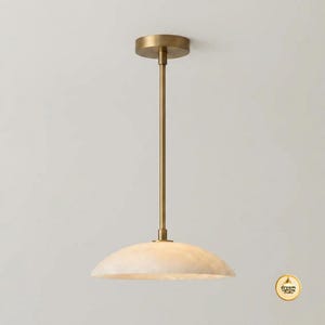 May include: A pendant light fixture featuring a circular brass canopy and a slender vertical rod in a matching brass finish. The light is completed by a wide, shallow, dome-shaped shade with a translucent, marbled off-white stone texture.