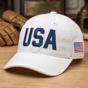 以下が含まれることがあります： 白の野球帽。 ネイビーブルーで「USA」の文字が刺繍されています。 帽子の側面には小さなアメリカ国旗のパッチが付いています。 帽子は丈夫な生地で作られており、つばがカーブしています。