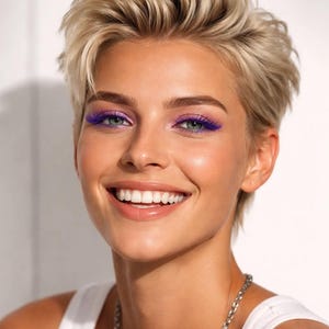 Può includere: Una persona sorridente con capelli biondi corti e vivace trucco viola sugli occhi. Indossa una canotta bianca e una collana a catena d'argento. Lo sfondo è un muro bianco.