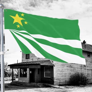 Può includere: Una bandiera verde e bianca con stelle gialle sventola al vento. La bandiera è montata su un palo d'argento davanti a un edificio in bianco e nero. Il design della bandiera include una sezione superiore verde con tre stelle gialle e strisce bianche e verdi.