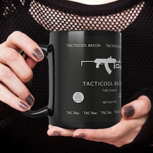 May include: Black ceramic mug with the text "TACTICOOL BACON" and a graphic of a firearm. The mug also includes the text "Fully Cooked" and "NET WT. 9 OZ."