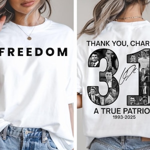 May include: White t-shirt with the word "FREEDOM" in bold black letters on the front. The back of the shirt features the text "THANK YOU, CHARLIE." with the number "31" and a signature, along with the words "A TRUE PATRIOT 1993-2025".