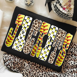 May include: Black sweatshirt with the word "JAGUARS" in a bold, stylized font. The letters are a mix of softball-themed designs, leopard print, and softball graphics. The sweatshirt is displayed on a white and leopard print surface.
