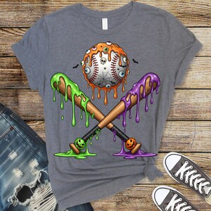 K&ouml;nnte beinhalten: Graues T-Shirt mit einem Halloween-Motiv. Das Design zeigt einen Baseball mit Aug&auml;pfeln, einem Spinnennetz und einem Totenkopf, gekreuzte Baseballschl&auml;ger mit gr&uuml;nem und lila Schleim und kleine Flederm&auml;use.