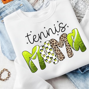 K&ouml;nnte beinhalten: Wei&szlig;es Sweatshirt mit dem Text "tennis mama" in schwarzer Schrift und fetten Buchstaben. Das Wort "mama" hat ein Leopardenmuster und Tennisballgrafiken. Die Buchstaben "M" sind mit Tennisballgrafiken gestaltet.