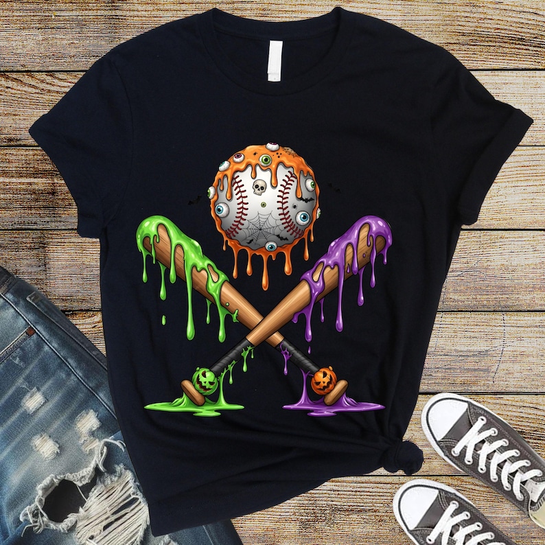 K&ouml;nnte beinhalten: Schwarzes T-Shirt mit einem Halloween-Motiv. Ein Baseball mit Augen und einem Spinnennetz wird von zwei Baseballschl&auml;gern gekreuzt, die mit gr&uuml;nem und lila Schleim tropfen. Die Schl&auml;ger haben K&uuml;rbisse an den Enden.