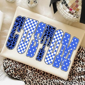 Puede incluir: Sudadera de color crema con la palabra "CUSTOM" en letras grandes y en negrita. Las letras presentan una mezcla de estampado de leopardo azul, patrones de cuadros blancos y azules y azul con estrellas blancas. La sudadera está doblada sobre una tela con estampado de leopardo.