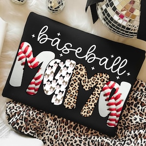 May include: Black sweatshirt with the words "baseball Mama" in white script. The word "Mama" is decorated with baseball stitching, bows, and leopard print. The sweatshirt is on a leopard print fabric.