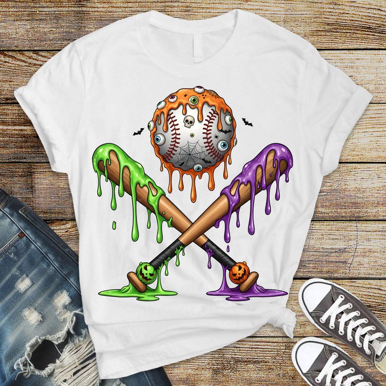 K&ouml;nnte beinhalten: Wei&szlig;es T-Shirt mit einem Halloween-Motiv. Die Grafik zeigt einen Baseball mit Aug&auml;pfeln, einem Spinnennetz und einem Totenkopf, gekreuzte Baseballschl&auml;ger mit gr&uuml;nem und lila Schleim und kleine K&uuml;rbisse.
