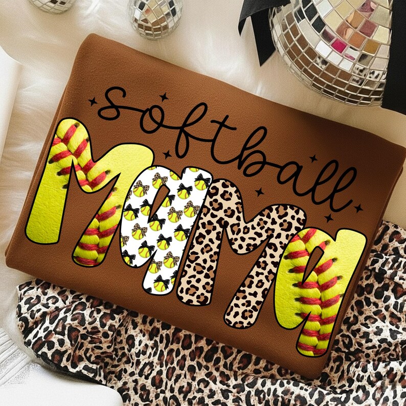 May include: Brown sweatshirt with the words "Softball Mama" in a mix of fonts and patterns. The word "Mama" features softball designs, leopard print, and softball stitching. The sweatshirt is a comfortable, casual style.
