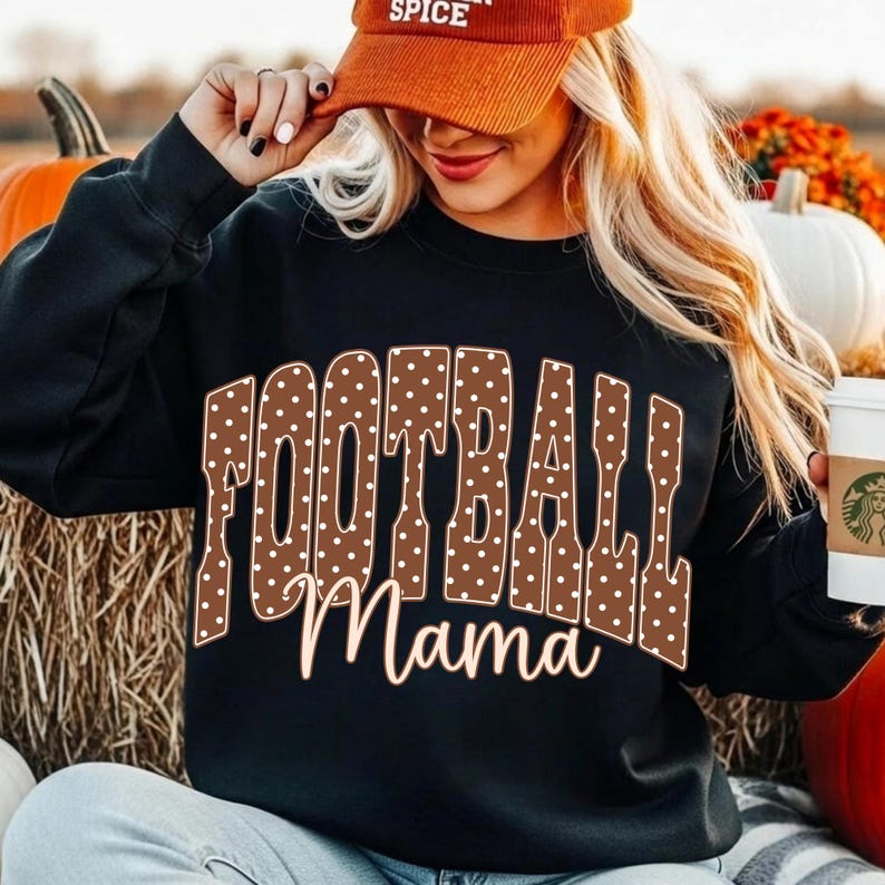 May include: A black long-sleeve sweatshirt featuring the word FOOTBALL in large brown letters with white polka dots, and the word Mama in a light-colored script font underneath. The garment is worn with an orange corduroy baseball cap.