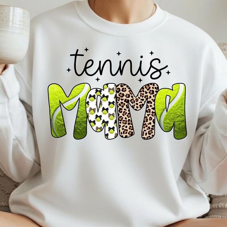 K&ouml;nnte beinhalten: Wei&szlig;es Sweatshirt mit dem Text "tennis Mama" in schwarzer Schrift und einem verspielten Design. Das Wort "Mama" zeigt ein Tennisball- und Leopardenmuster. Das Sweatshirt ist ein bequemer, l&auml;ssiger Stil.