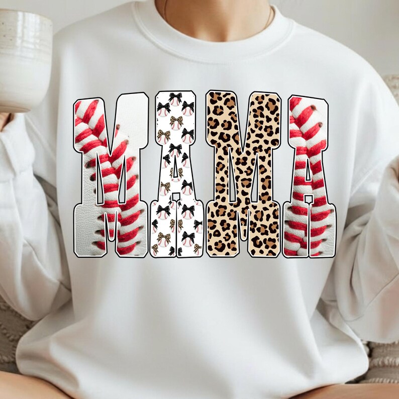 May include: White sweatshirt with the word "MAMA" in a bold, outlined font. The "M" and "A" are designed with baseball stitching, the second "M" has a leopard print, and the second "A" has a pattern of bows and baseballs.