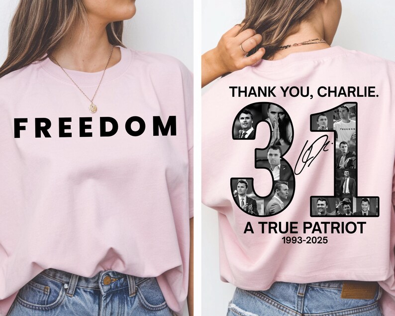 May include: Light pink t-shirt with the word "FREEDOM" in large black letters. The back of the shirt features the text "THANK YOU, CHARLIE." and the number "31" with images of a person. The text "A TRUE PATRIOT 1993-2025" is also printed.