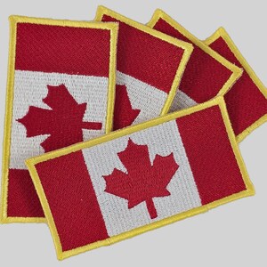 May include: Embroidered patches featuring the Canadian flag. Each patch has a red and white design with a red maple leaf in the center. The patches are rectangular with a yellow border. The patches are suitable for clothing or accessories.