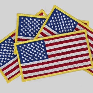 May include: A collection of embroidered American flag patches. Each patch features a blue field with white stars and red and white stripes, outlined with a yellow border. The patches are arranged in a slightly overlapping pattern.