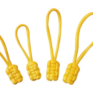 May include: Four yellow zipper pulls with knotted ends and looped cords. The pulls are in varying sizes, all with a bright, sunny colour. The knotted ends are cylindrical, and the loops are made of the same material.