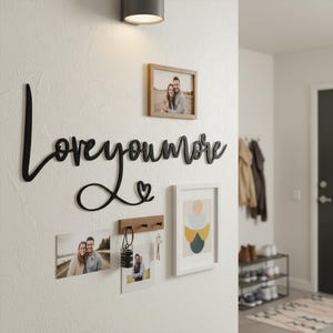 May include: A wall-mounted display featuring a black metal "love you more" sign, framed photos, and a key holder. The photos are in wooden and white frames. A modern wall sconce is mounted above the display.