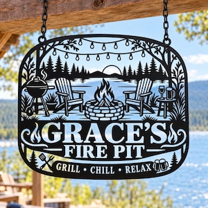 May include: A black metal hanging sign featuring a laser-cut design of a fire pit, two chairs, a grill, and string lights. The text reads GRACE'S FIRE PIT and GRILL • CHILL • RELAX. The sign is suspended by two black chains from a wooden beam.