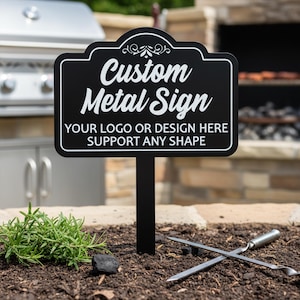 May include: A black metal sign with white text reading "Custom Metal Sign" and "Your logo or design here support any shape." The sign is in a garden setting. Two metal skewers are crossed in front of the sign. A barbecue grill is visible in the background.