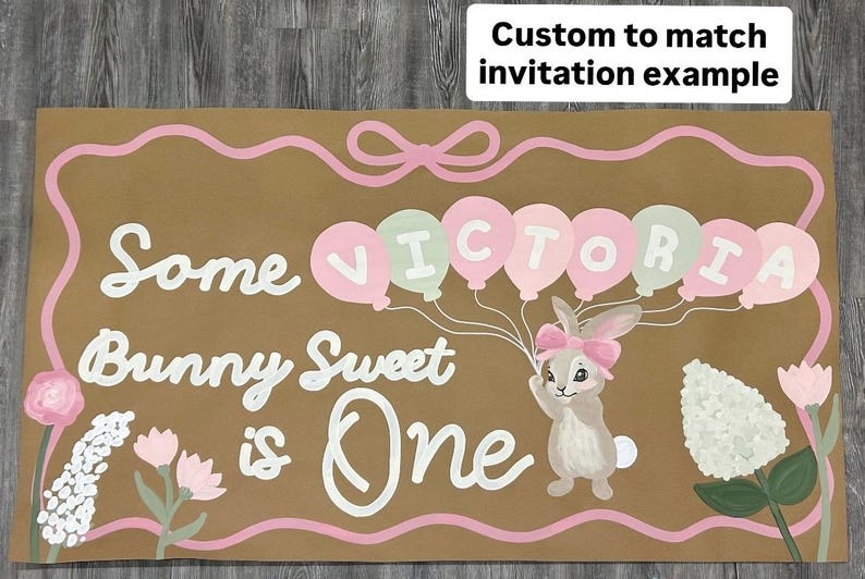 May include: A rectangular brown sign featuring the white text Some Bunny Sweet is One, a pink bow border, a bunny with a pink bow, and balloons spelling VICTORIA in alternating pink and light green. The sign includes floral illustrations.