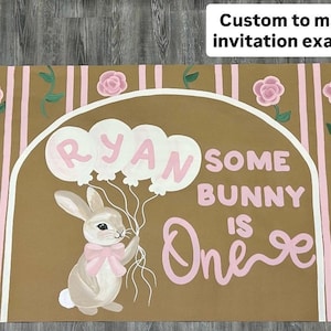 May include: A rectangular sign with a tan background featuring vertical pink stripes and pink roses on vines. A white arch frames a bunny holding balloons with the name RYAN and the text SOME BUNNY IS ONE. A text box reads Custom to match invitation example.