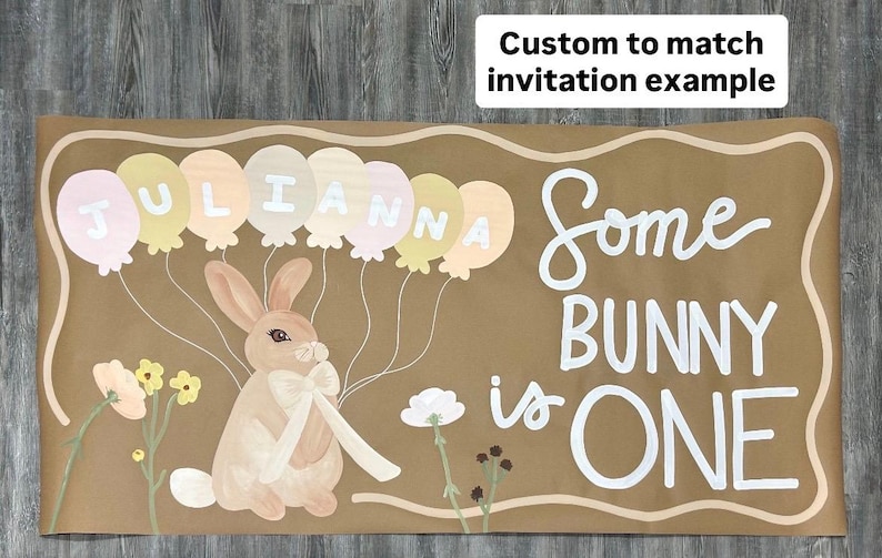 May include: A rectangular brown banner featuring a painted rabbit with a white bow, surrounded by pastel balloons spelling JULIANNA and the white text Some BUNNY is ONE. A white box in the corner contains the text Custom to match invitation example.